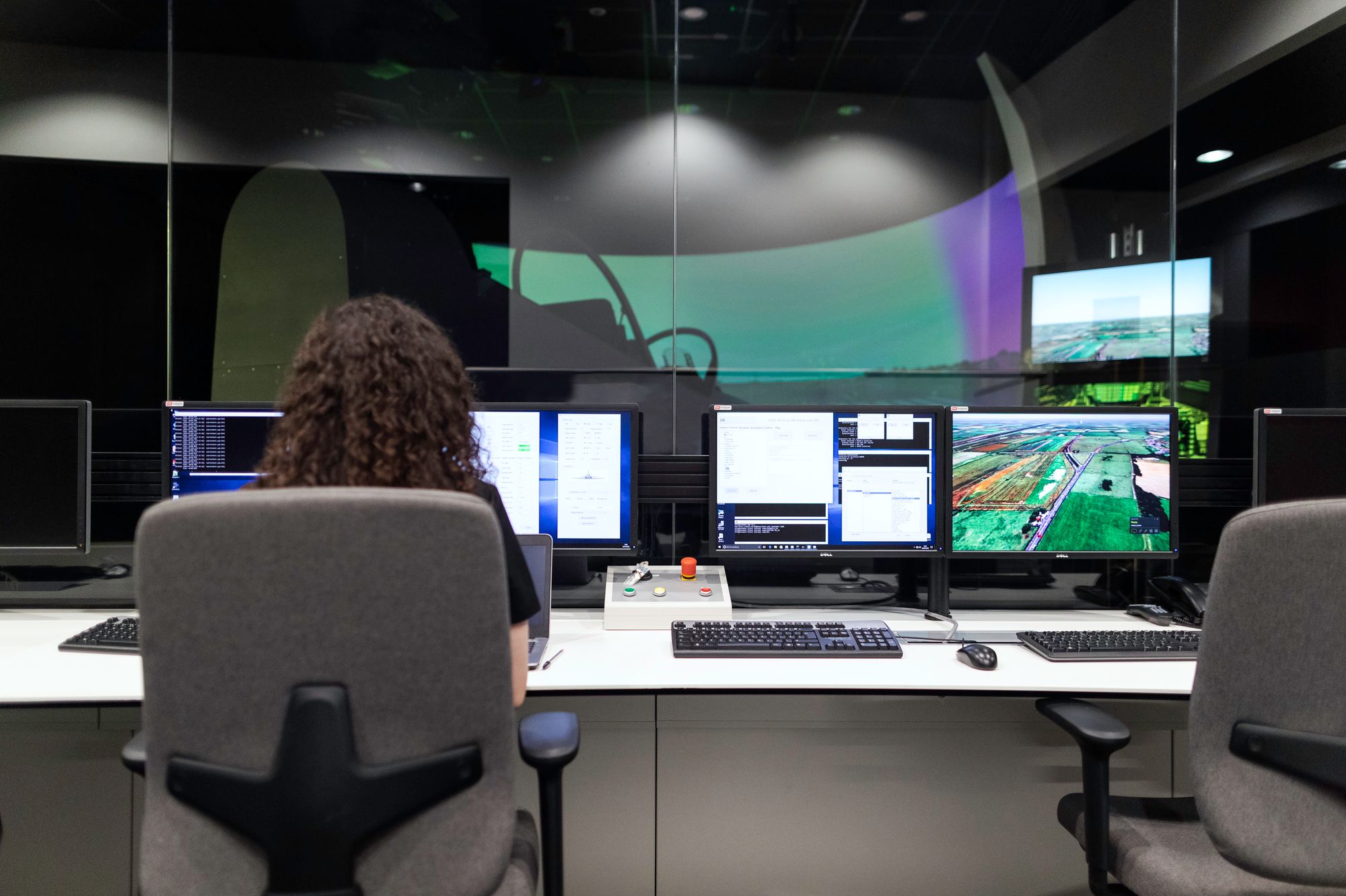 An operator at a row of monitors showing a map, in a darkened control room