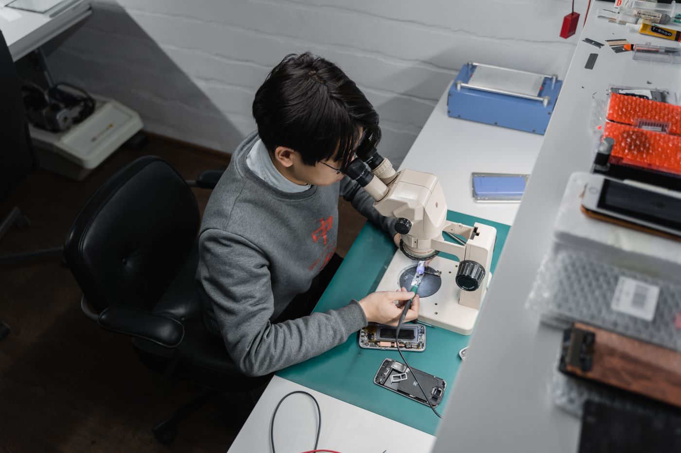 A technician inspecting a device under a microscope at a workbench