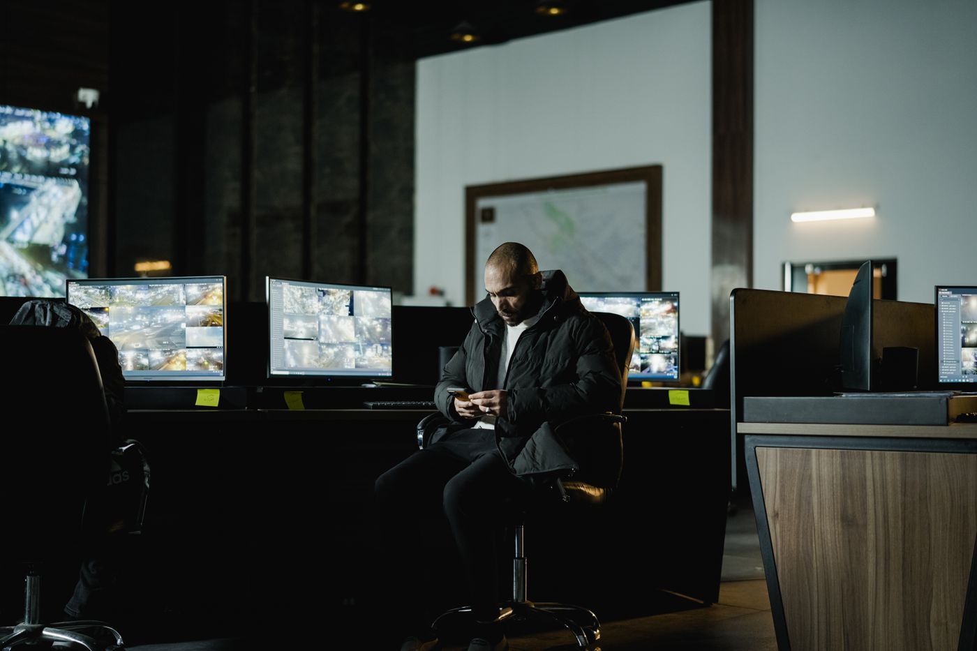 An operator at a desk of screens in a control room, with a city map on the wall behind